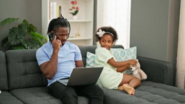 Afrikalı Amerikalı baba ve kız kanepede oturuyor ve evde çalışıyor.