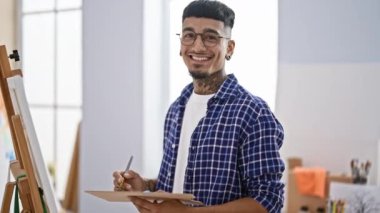 Gülümseyen, kendine güveni tam bir Latin sanatçı resim stüdyosunda çizim yapmakla, sanatsal yaratıcılığını kullanmakla meşgul.