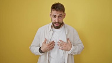 Neşeli, genç, İspanyol asıllı bir adam güvenli bir şekilde konuşuyor, izole edilmiş sarı bir arka plana neşe ve pozitiflik saçıyor, moda anlayışı ve bulaşıcı gülümsemesiyle mutluluğu somutlaştırıyor..