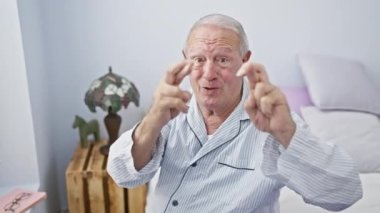 Pijamalı neşeli adam, şans umuduyla, yatakta oturuyor, gözleri kapalı, parmaklarını çapraz yapıyor yatak odasında..