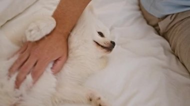 Yatak odasında köpekli beyaz bir adam oturuyor.