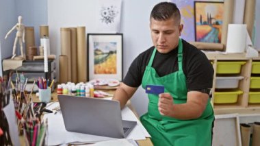 Çalışkan Latin sanatçı, kariyerinin sorumluluklarını üstlenen genç adam. Sanat stüdyosunda dizüstü bilgisayar ve kredi kartıyla.