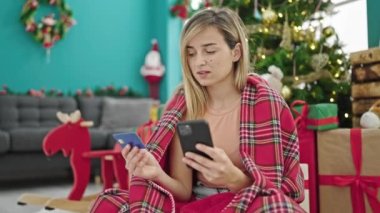 Akıllı telefon ve kredi kartıyla alışveriş yapan genç sarışın kadın Noel 'i evde kutluyor.