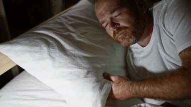 Kafkasyalı bir adam yatak odasında uyumak için yatağa uzanıyor.