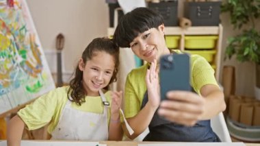 Anne-kız kaynaşması, kadın sanatçı öğretmen ve genç kız öğrenci iç mekan sanat dersi sırasında bir araya gelir, canlı stüdyo ortamında gülümser ve paylaşırlar.