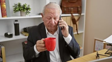 Kendine güvenen kıdemli bir adam telefonda konuşurken gülümsüyor. Ofiste kendine güvenerek espresso yudumluyor..