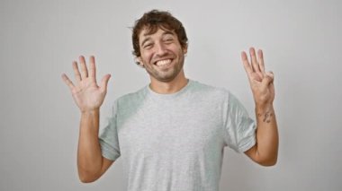 Sekiz numaralı tişörtlü neşeli genç adam el hareketlerini göstererek kendini gösteriyor. İzole edilmiş beyaz bir arkaplanda mutlu bir gülümseme