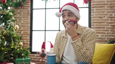 Genç İspanyol adam akıllı telefonuyla sesli mesaj gönderiyor evde Noel 'i kutlamak için kahve içiyor.