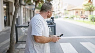 Yakışıklı, orta yaşlı, havalı ve rahat bir yüzü olan beyaz bir adam. Açık havada akıllı telefon kullanıyor, şehirde taksi arıyor.