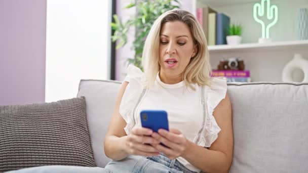 Mladá Blondýna Žena Pomocí Smartphone Sedí Pohovce Myšlení Doma — Stock video