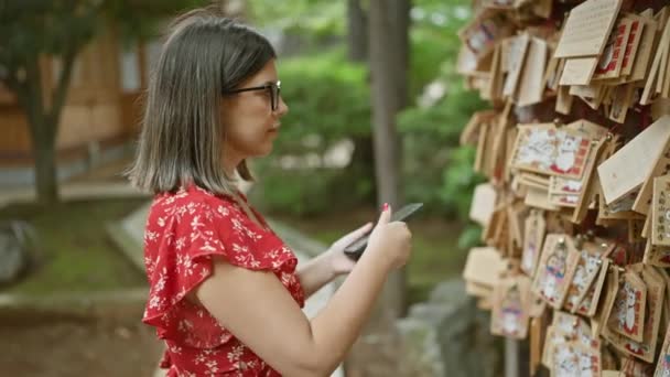 在日本的Gotokuji庙宇里 戴眼镜的美丽女人用智能手机镜头抓拍到了一个祈祷板 保持了传统 — 图库视频影像