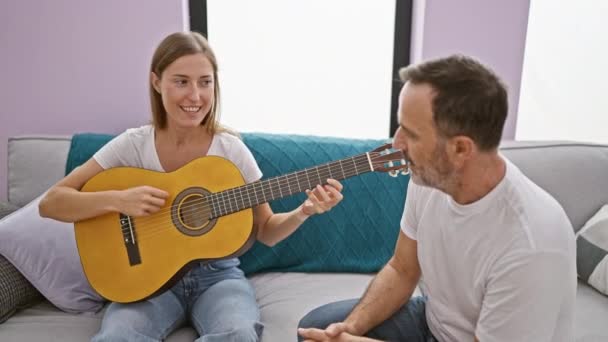在舒适的客厅里 父亲和女儿坐在沙发上弹奏古典吉它时 彼此依偎在一起 他们随意的表情闪烁着爱与悠闲的光芒 — 图库视频影像