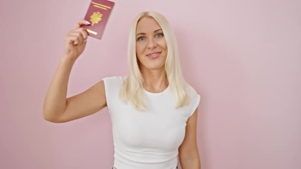 欢快的金发姑娘摇曳着法国护照 带着欢乐的笑容 带着粉红孤寂的背景 相信她的旅行一定会成功 — 图库视频影像