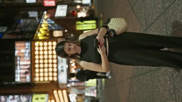 美しいヒスパニック女性が東京の街灯で笑顔でスマートフォンで幸せにテキストを送る — ストック動画