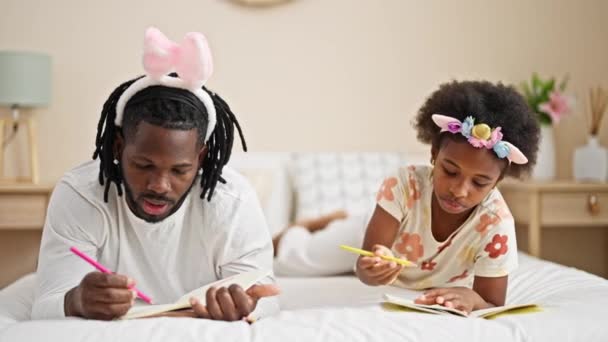 アフリカ系アメリカ人の父親と娘は寝室のベッドに横たわるノートブックに面白い日記を着ています — ストック動画