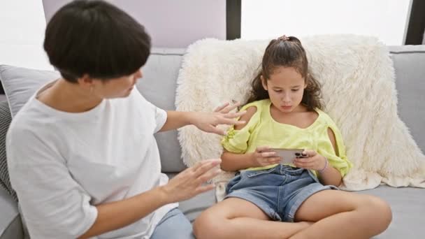 松懈的母亲和女儿舒适地坐在舒适的沙发上 诚恳地要求家里有智能手机 — 图库视频影像