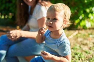 Anne ve oğlu bankta oturup parkta küçük solucanlar yiyorlar.