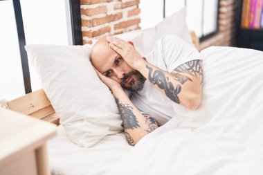 Young bald man stressed sitting on bed at bedroom