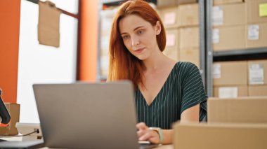 Genç kızıl saçlı kadın iş kadını ofiste dizüstü bilgisayar kullanıyor.