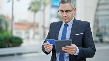 Sokakta dokunmatik ped ve kredi kartı kullanan Latin kökenli genç bir iş adamı.