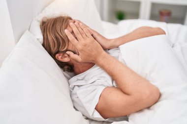 Yatak odasında yatan genç sarışın stresli bir adam.