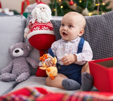 Evdeki Noel ağacının yanında kendine güvenen sevimli, beyaz bir bebek oturuyor.