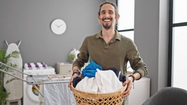 Çamaşır odasında çamaşır sepetini tutan kendine güvenen İspanyol genç adam.