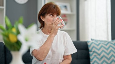 Orta yaşlı bir kadın kanepede oturmuş su içiyor.