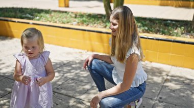 Kendine güvenen anne ve neşeli kızı parkın yemyeşil sularında birlikte gülümsüyor.