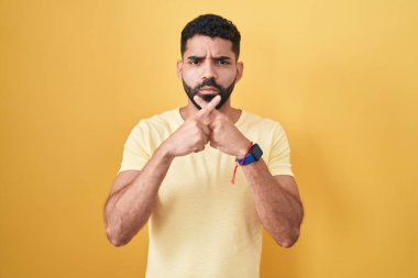 Hispanic man with beard standing over yellow background rejection expression crossing fingers doing negative sign 