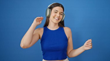 Genç, güzel İspanyol kadın müzik dinliyor ve izole edilmiş mavi arka planda dans ediyor.