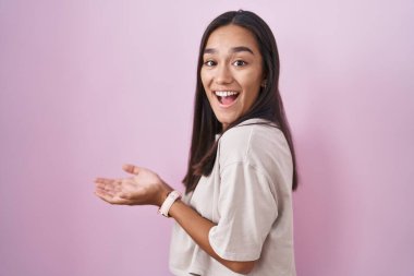 Pembe arka planda duran genç İspanyol kadın avuçlarını açıp fotokopi alanını gösteriyor, gülümseyerek mutlu bir şekilde gülümsüyor. 
