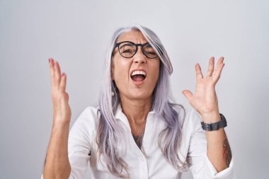 Beyaz arka planda gözlük takan orta yaşlı bir kadın deli deli deli bağırıyor ve agresif bir ifade ve kollarla bağırıyor. hüsran kavramı. 