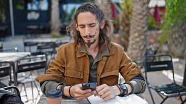 Kahve dükkanının terasında akıllı telefon kullanan genç İspanyol turist.