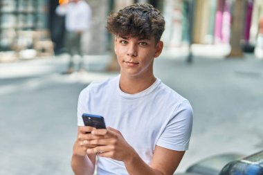 Latin kökenli genç sokakta rahat bir ifadeyle akıllı telefon kullanıyor.