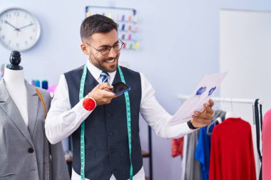 Genç İspanyol terzi akıllı telefondan konuşuyor terzi dükkanında kıyafet tasarımı yapıyor.