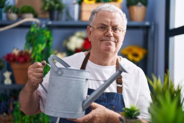 Çiçekçide çiçekleri sulayan kır saçlı bir adam.