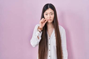 Çinli genç bir kadın pembe arka planın başında duruyor. Ağzı ve dudakları parmakları fermuar gibi kapalı. gizli ve sessiz, tabu konuşması 