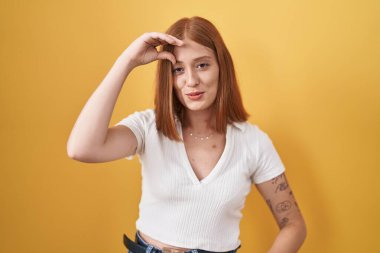 Sarı arka planda dikilen genç kızıl saçlı kadın endişeli ve stresli. Alnındaki bir sorun yüzünden gergin ve bunalımda. 