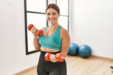 Spor merkezinde dambılları kullanarak gülümseyen güzel bir İspanyol kadın.