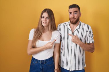 Sarı arka planda dikilen genç çift endişeli ve endişeli bir ifade sergiliyor. 