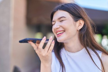 Beyaz bir kadın gülümsüyor ve caddede akıllı telefondan konuşuyor.