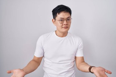 Beyaz arka planda duran Asyalı genç adam habersiz ve kolları açık, hiçbir fikri yok.. 