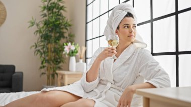 Bornoz giymiş genç ve güzel bir İspanyol kadın yatak odasında şampanya içiyor.