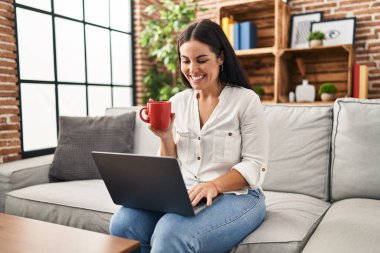 Genç ve güzel İspanyol kadın dizüstü bilgisayar kullanıyor. Evde kahve içiyor.