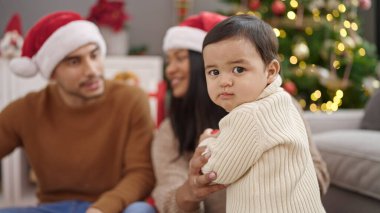 Evde Noel ağacının yanında oturmuş kendinden emin bir şekilde gülümseyen bir çift ve oğul.