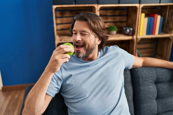 Middle age man eating apple sitting on sofa at home