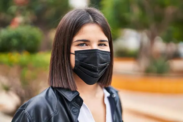 Genç, güzel, İspanyol bir kadın parkta maske takarak gülümsüyor.