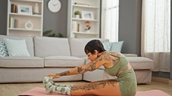 Hispanic woman with amputee arm sitting on floor stretching legs at home