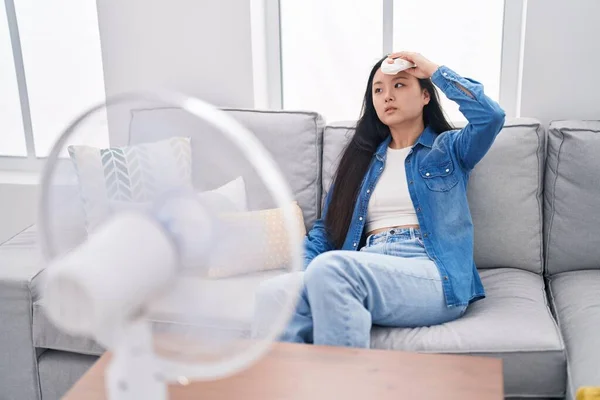 Young chinese woman using ventilator sitting on sofa at home